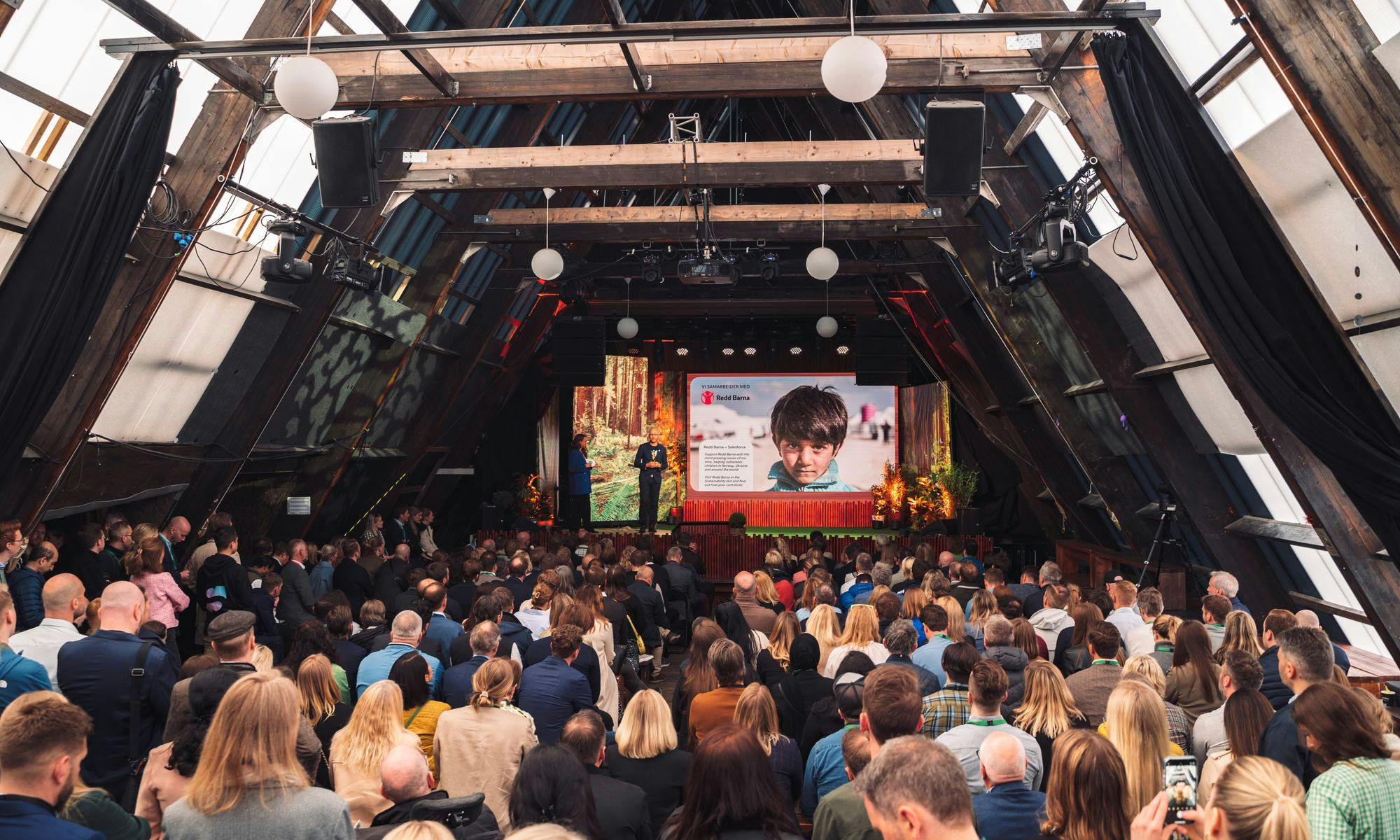 Bilde av SALT oslo, stor sal med flere personer, samt scene og LED skjerm. 