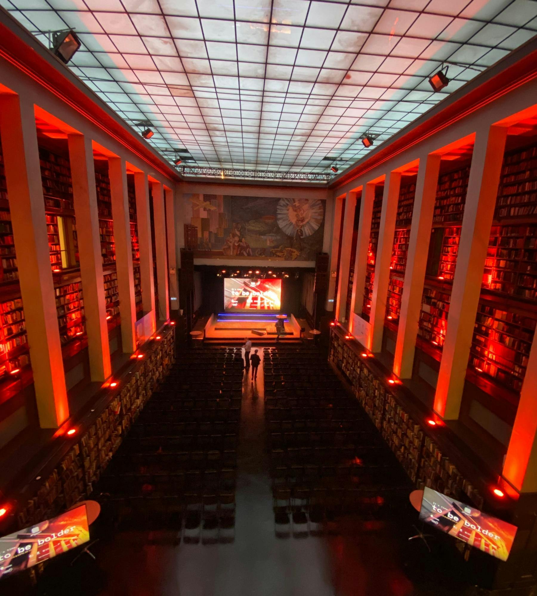 Stor ærverdig sal med rødt lys og scene og LED skjerm i den ene endren. Foto. 