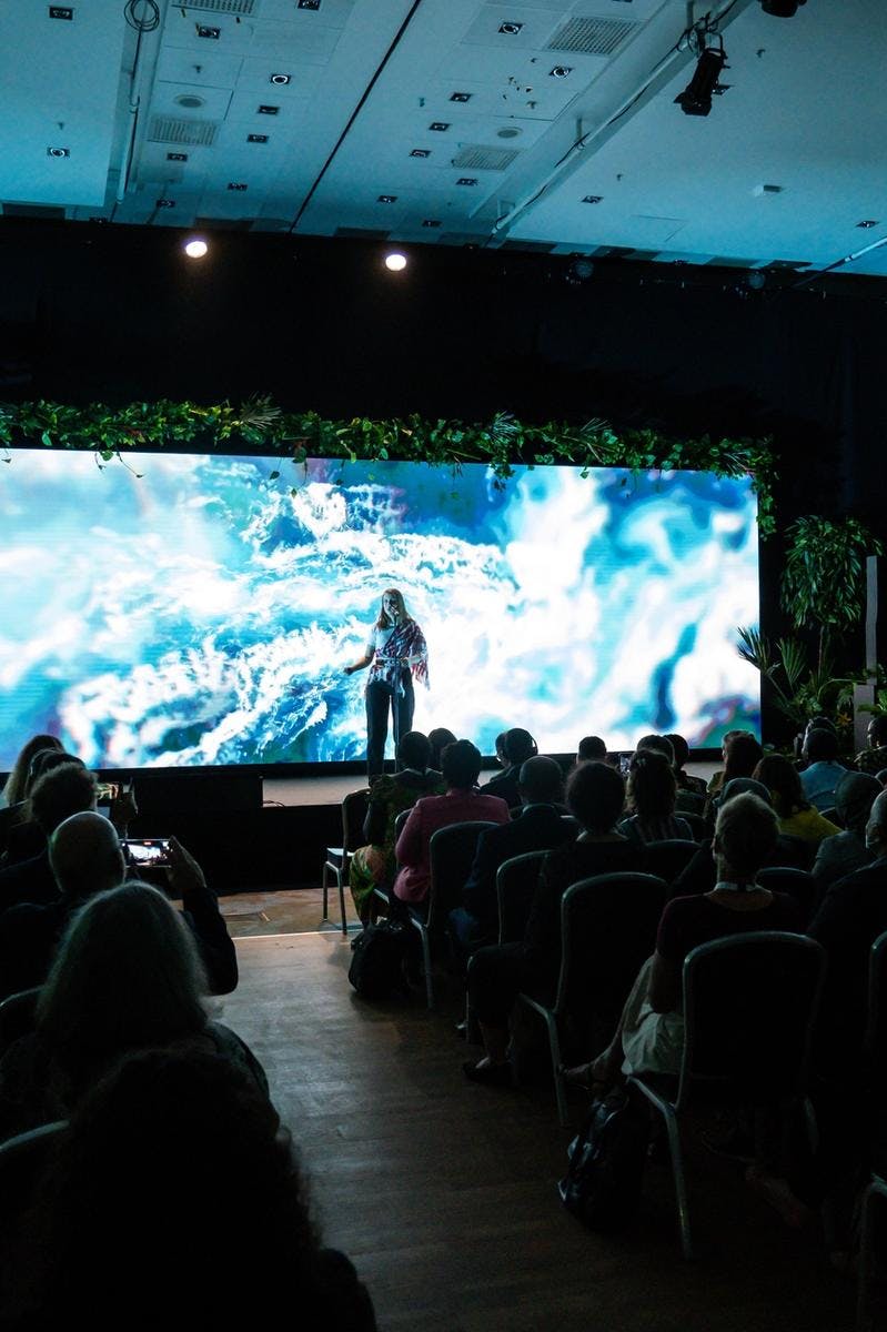 Artist står på en scene med grafisk innhold på LED skjerm bak seg. Mørklagt sal. Foto